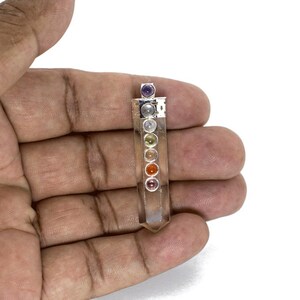 May include: A clear quartz crystal pendant with seven chakra stones embedded in silver settings. The stones are red, orange, yellow, green, blue, indigo, and violet.