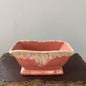 May include: A rectangular, coral-colored ceramic planter with a white, textured rim. The planter sits on a small, matching base. The interior is a solid coral color, and the exterior has a glossy finish.