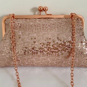 May include: A rose gold sequined clutch with a rose gold chain strap. The clutch has a clasp closure.