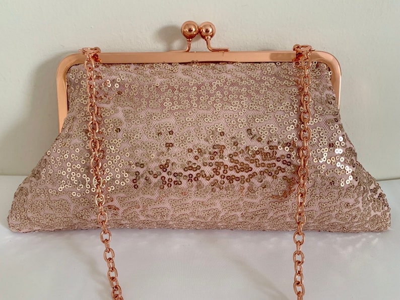 May include: A rose gold sequined clutch with a rose gold chain strap. The clutch has a clasp closure.