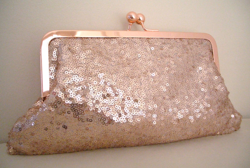 May include: A rose gold clutch purse covered in sequins. The purse has a metal clasp closure.