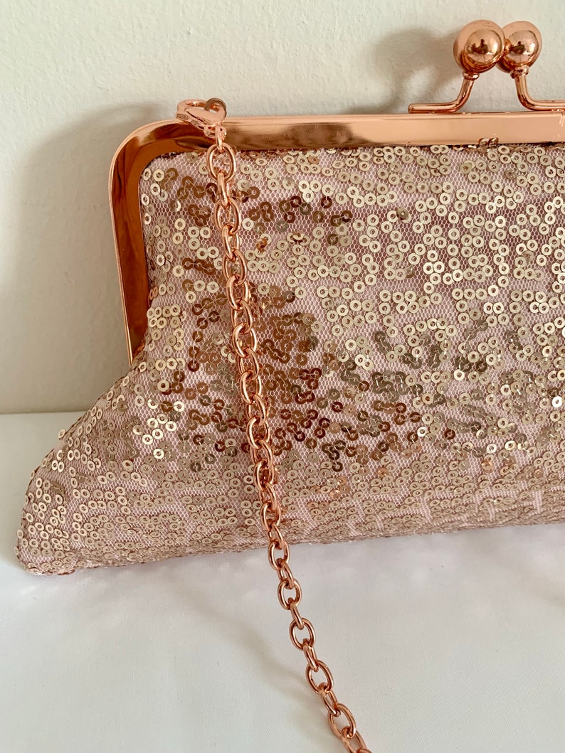 May include: A rose gold clutch purse with a chain strap and a sequined fabric. The purse has a clasp closure.