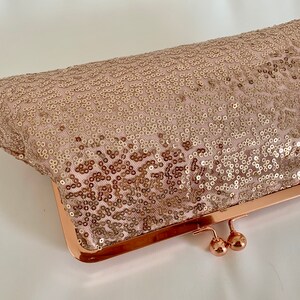 May include: A rose gold sequined clutch purse with a metal frame and clasp.