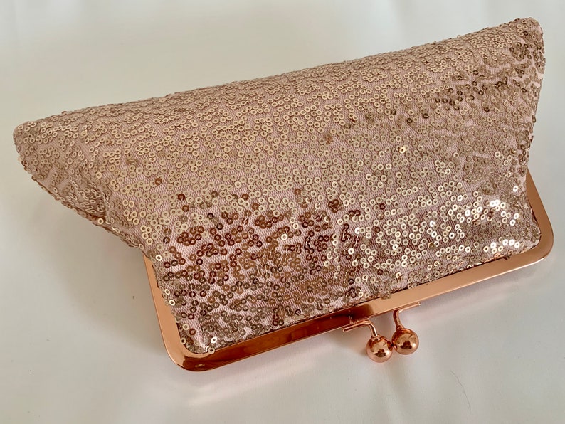 May include: A rose gold sequined clutch purse with a metal frame and clasp.