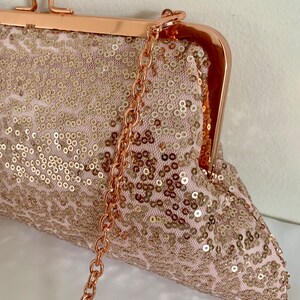 May include: A rose gold sequined clutch with a chain strap. The clutch has a clasp closure and is decorated with sequins.