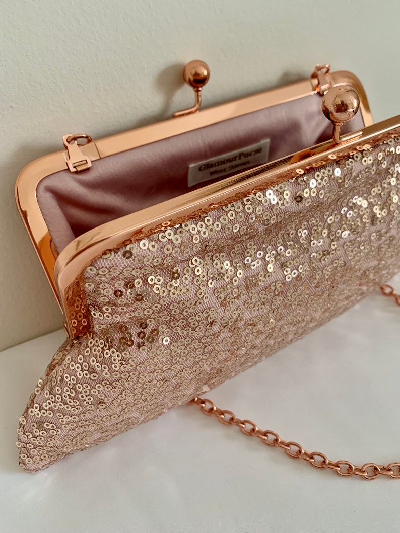 May include: A rose gold clutch purse with a chain strap. The purse is covered in sequins and has a satin lining. The purse has a clasp closure and the brand name "Glamour Purse" is printed on the inside.