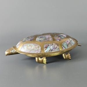 May include: A brass turtle trinket box with a shell inlaid with iridescent mother-of-pearl. The turtle has four legs and a detailed head.