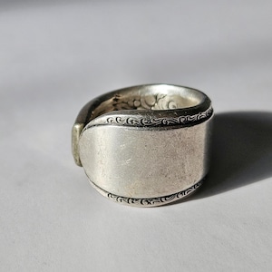 Può includere: Un anello a forma di cucchiaio d'argento con un design decorativo sul bordo.