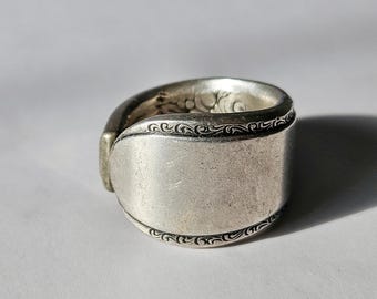 May include: A silver spoon ring with a decorative design around the edge.