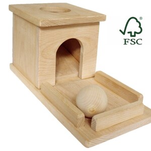 May include: A natural wood toy with a rectangular base, a small archway, and a circular opening on top. A wooden ball rests on a track in front of the structure. The FSC logo is visible.