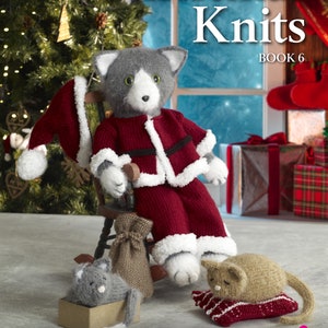 May include: The cover of a knitting pattern book titled "Christmas Knits Book 6" features a knitted cat dressed as Santa Claus. The cat is wearing a red suit with white trim and a matching hat. Other knitted cat figures and accessories are also shown.
