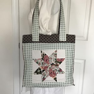 May include: A quilted tote bag with a star design. The bag features a light blue and white gingham pattern, a brown floral pattern, and a central star made of floral fabric. The handles are light blue and white gingham.