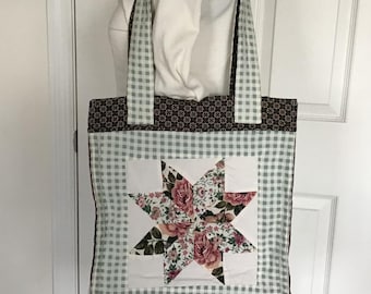 May include: A quilted tote bag with a star design. The bag features a light blue and white gingham pattern, a brown floral pattern, and a central star made of floral fabric. The handles are light blue and white gingham.