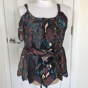 May include: A patterned top with a unique design. The top features a mix of colors including teal, purple, and black. It has a wrap-around tie at the waist and cold shoulder sleeves. The fabric has a silky appearance.