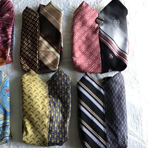 May include: Six pouches crafted from repurposed neckties, each featuring two distinct fabric patterns joined together. The designs include various geometric, floral, and striped motifs in colors such as black, pink, brown, yellow, blue, and grey.