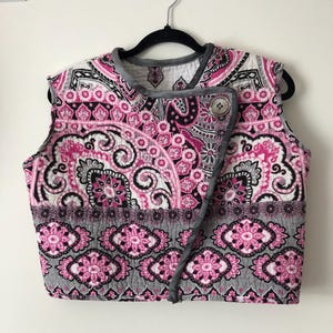 May include: A sleeveless vest with a pink and black paisley pattern. The vest has a button closure and a gray trim.