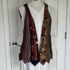 May include: A sleeveless vest constructed from multiple neckties featuring various patterns and colors, including deep red with white geometric shapes, a black and red plaid design, a floral print with gold and brown, and a brown woven texture.