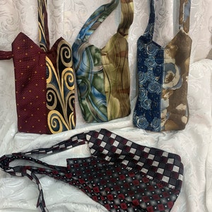 May include: Five small bags made from repurposed neckties. The bags are in various colors and patterns, including red, gold, blue, green, and brown. The bags have a strap and are designed to be worn as a crossbody bag.