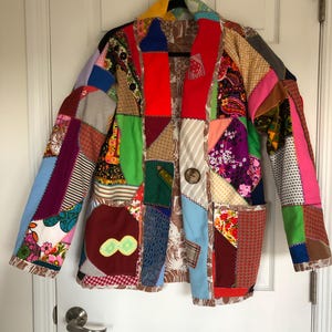 May include: A colorful patchwork jacket with a variety of fabrics and patterns, including floral, geometric, and plaid. The jacket has a button closure and long sleeves.