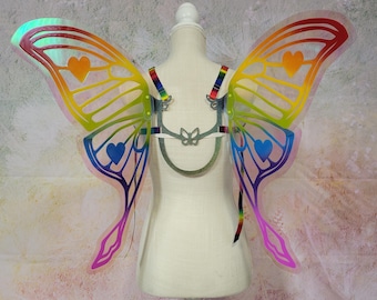 May include: Rainbow iridescent butterfly wings with heart cutouts. The wings are attached to a silver metal harness with adjustable straps.