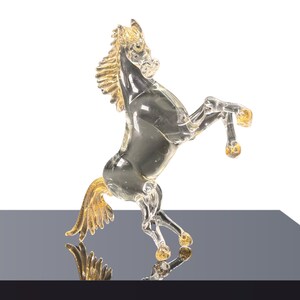 Peut inclure: Figurine de cheval en verre transparent cabré sur ses pattes arrière. La crinière, la queue et les sabots sont dorés. Le cheval est présenté sur une surface réfléchissante sur fond blanc.