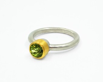 May include: A silver ring with a green gemstone set in a gold bezel. The ring is simple and elegant.