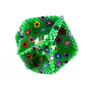 May include: A green beaded cube with a floral pattern. The cube is made of small, colorful beads that are arranged in a repeating pattern of flowers.