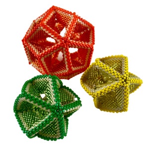 Op de afbeelding: Drie geometrische kralenversieringen in rood, geel en groen. Elk ornament is gemaakt van kleine kralen die samen geweven zijn in een complex patroon om een driedimensionale vorm te creëren.