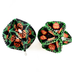Puede incluir: Dos adornos de cuentas en forma de cubo, con un esquema de color negro, verde y naranja. Los adornos están hechos de cuentas pequeñas y tienen un diseño geométrico.