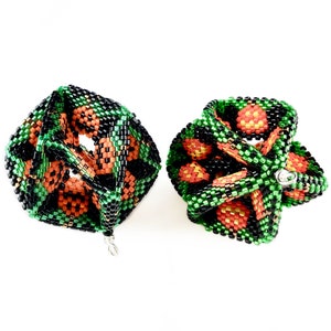 Peut inclure: Deux ornements en perles en forme de cube, avec un schéma de couleurs noir, vert et orange. Les ornements sont faits de petites perles et ont un design géométrique.