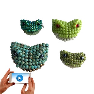 May include: Four beaded frog faces, two green, one turquoise, and one light green. The frogs have black eyes and are all smiling.