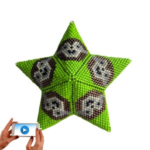 May include: A green star-shaped ornament with five brown and white animal faces on each point. The ornament is made of beads and is a handmade craft.