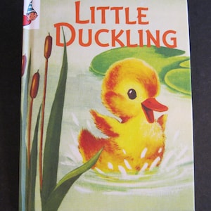 May include: A vintage children's book titled "Little Duckling." The cover features a yellow duckling with an orange beak and accents, splashing in water. The background includes green lily pads and reeds. A small cartoon character is in the upper left corner.