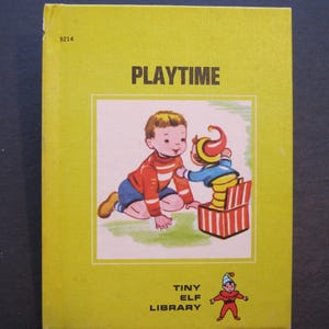 May include: A yellow book with the title "PLAYTIME" and a picture of a child playing with a jack-in-the-box toy. The book is part of the "Tiny Elf Library" series.