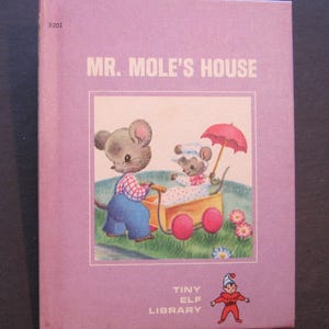 May include: A purple book with the title "Mr. Mole's House" on the cover. The cover features an illustration of two mice, one pushing a stroller with a baby mouse inside, and the other holding an umbrella. The book is part of the "Tiny Elf Library" series.