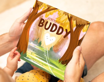 May include: A children's book titled "Remembering Buddy" held by a person. The cover features a heart-shaped character emitting light, set in a forest scene with the title in large, brown letters. The illustration has a warm, inviting color palette.
