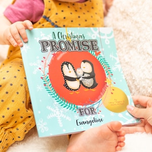 May include: A blue and red children's book titled "A Christmas Promise for Evangeline" with a penguin family illustration on the cover.