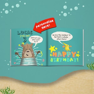 May include: Open book with a teal background, featuring a cartoon bear and the text "LUCAS you are 3". The right page says "HAPPY BIRTHDAY!" with a yellow bird and stars. A red arrow says "Personalise Here!"