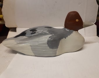 Puede incluir: Un señuelo de pato de madera pintado a mano con un cuerpo gris, blanco y negro y una cabeza roja. El señuelo está acostado de lado.