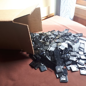 May include: A cardboard box overflowing with a large pile of black and grey plastic keyboard keys.