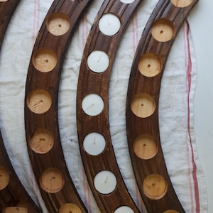 Op de afbeelding: Vier houten kaarsenstandaards met een gebogen vorm en meerdere kaarsvakken. Elke standaard heeft een donkerbruine vlek en is gemaakt van natuurlijk hout.