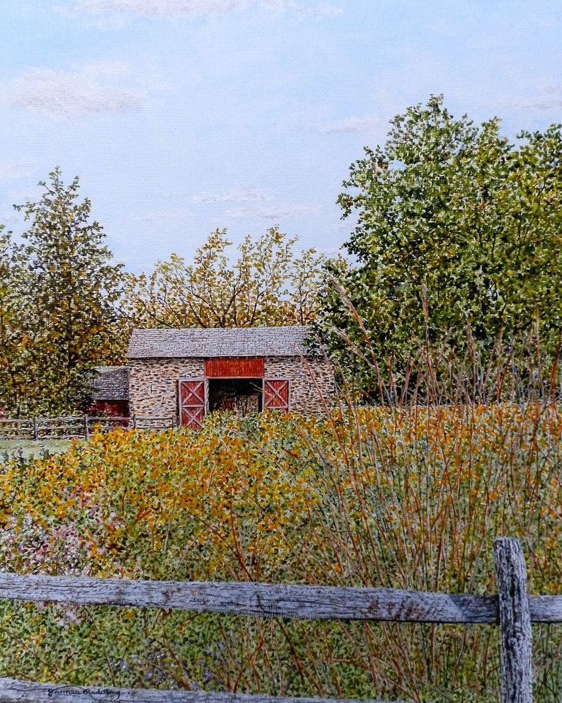 May include: A stone barn with a red door and a wooden fence in front of it. The barn is surrounded by trees and bushes. The sky is blue and cloudy.