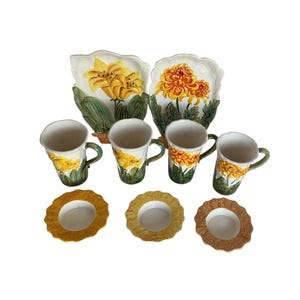May include: A ceramic floral tea set with yellow and orange flower designs. The set includes four mugs, three saucers, and two decorative plates. The mugs have green handles and the plates have a scalloped edge.