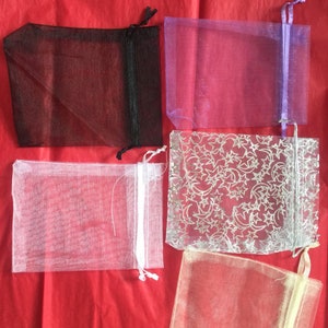 K&ouml;nnte beinhalten: F&uuml;nf Organza-Beutel in verschiedenen Farben. Die Beutel sind aus durchsichtigem Stoff und haben einen Kordelverschluss. Die Beutel sind in folgenden Farben erh&auml;ltlich: Schwarz, Lila, Wei&szlig;, Silber mit Sternenmuster und Beige.