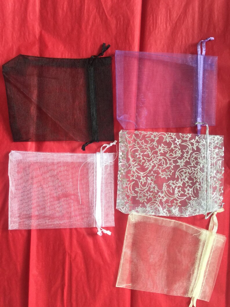 K&ouml;nnte beinhalten: F&uuml;nf Organza-Beutel in verschiedenen Farben. Die Beutel sind aus durchsichtigem Stoff und haben einen Kordelverschluss. Die Beutel sind in folgenden Farben erh&auml;ltlich: Schwarz, Lila, Wei&szlig;, Silber mit Sternenmuster und Beige.
