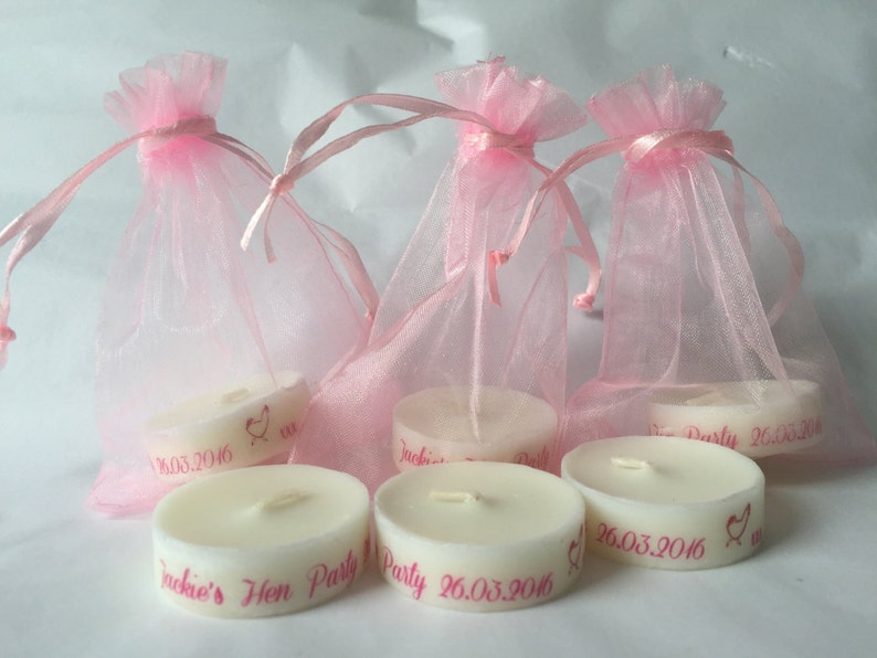 K&ouml;nnte beinhalten: Sechs kleine wei&szlig;e Kerzen mit rosa Beschriftung. Die Kerzen befinden sich in rosa Organzas&auml;ckchen. Der Text auf den Kerzen lautet "Jackie's Hen Party 26.03.2016".