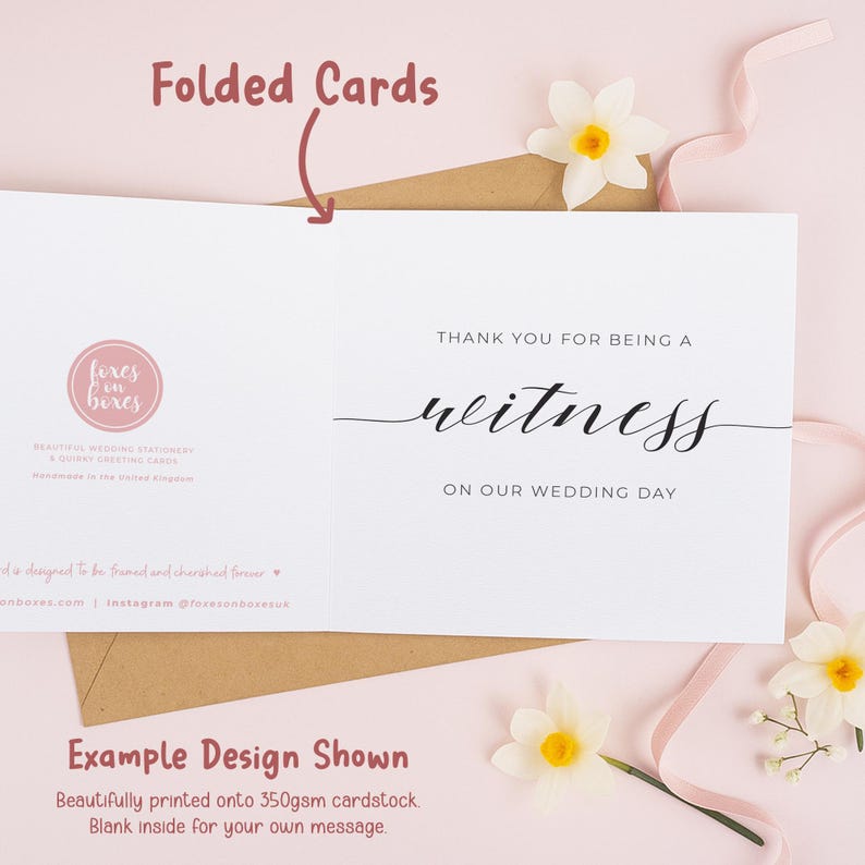 a white card with black text, a folded card, and some flowers on a pink background.