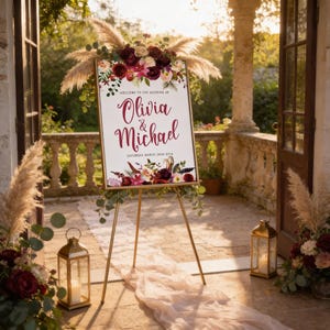 a wedding sign with floral decorations and lanterns, set up on a porch with a stone railing and a stone wall in the background.