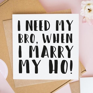 May include: A square white greeting card with bold black text that reads I NEED MY BRO, WHEN I MARRY MY HO! The card is positioned on top of a brown cardboard envelope, featuring a clean, minimalist design with clear, sans-serif lettering.