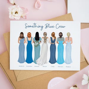 Op de afbeelding: Een rechthoekige kaart met de tekst Something Blue Crew boven een illustratie van zeven personen van achteren gezien. Ze dragen vloerlange jurken in verschillende tinten blauw en wit, met de namen Margot, Susanna, Hanna, Kellie, Cara, Nicola en Pamela onder elke figuur gedrukt.